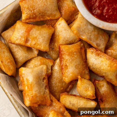 Golden brown and perfectly crispy pizza rolls cooked in an air fryer, presented on a plate alongside a savory bowl of pizza dipping sauce.