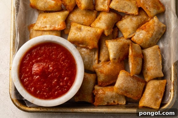 A plate full of golden, crispy air-fried pizza rolls, accompanied by a small bowl of pizza sauce for dipping.