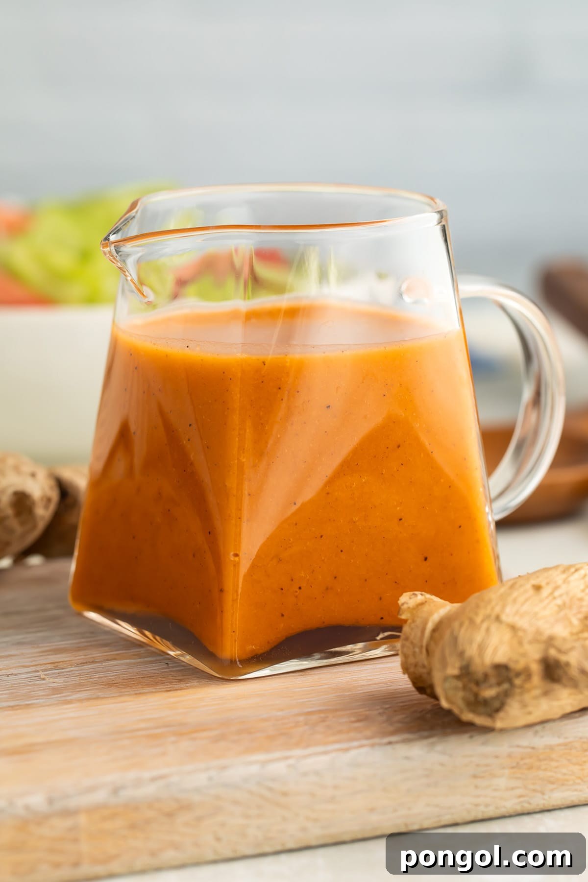 Homemade Ginger Salad Dressing 3 Close-up shot of the creamy, orange-hued ginger salad dressing in a clear glass pitcher, with a vibrant green salad visible in the background. The scene exudes freshness and inviting flavors.