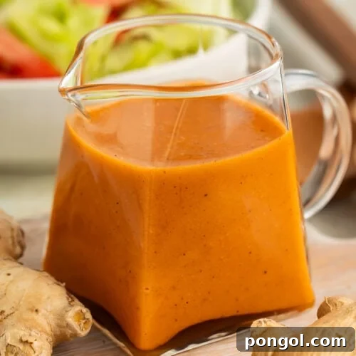 Vibrant orange-colored creamy ginger salad dressing, presented elegantly in a small clear glass pitcher.