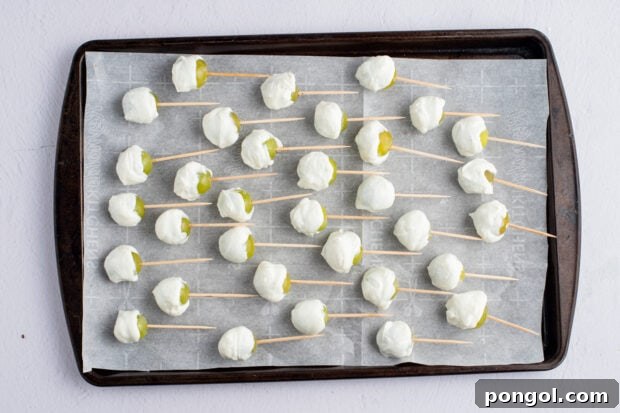 Yogurt-covered grapes, each with a toothpick, meticulously lined up on a baking sheet with parchment paper, ready for the final freeze.