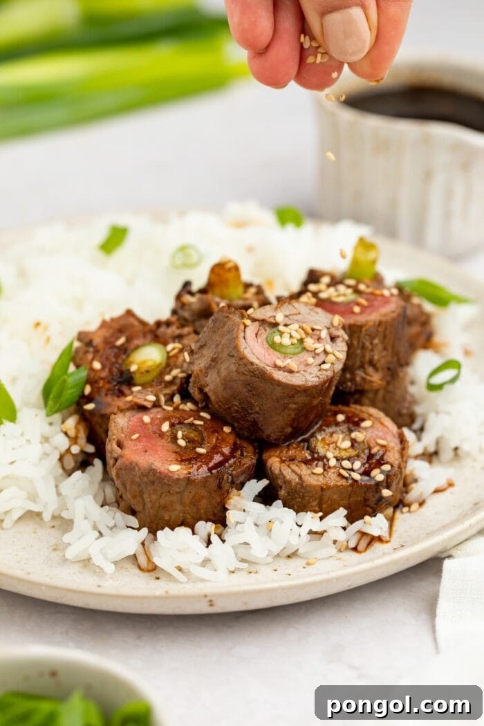 Tender beef negimaki rolls on a plate, garnished with sesame seeds and served with white rice