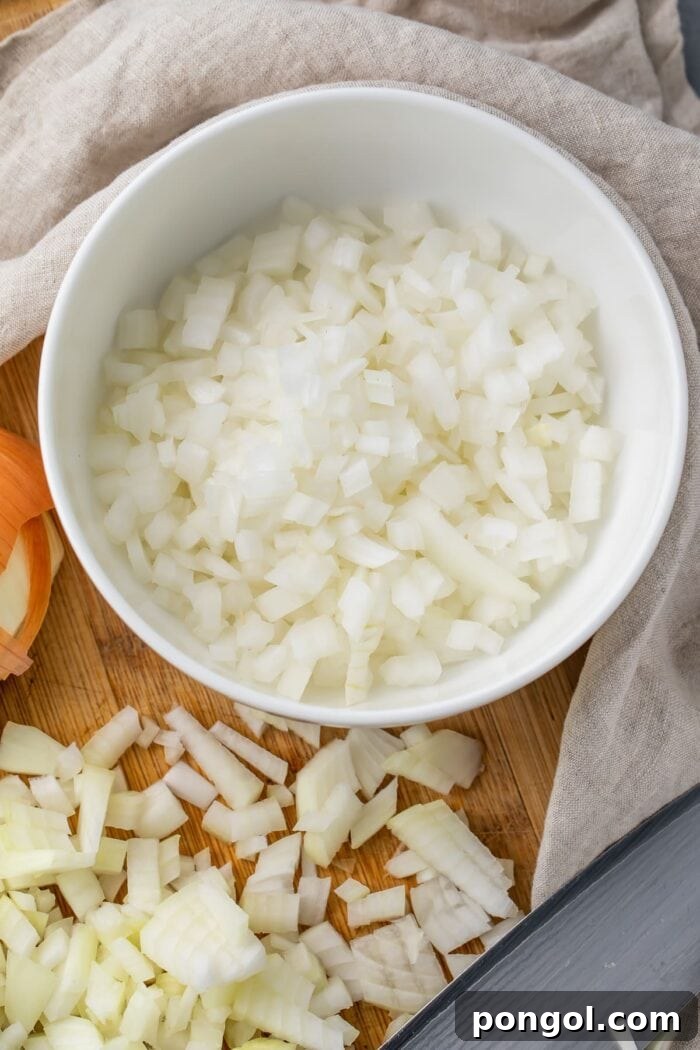 Diced onion on a cutting board next to a bowl of diced onion
