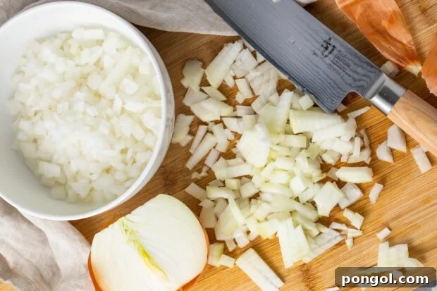 Diced onion on a cutting board next to a bowl of diced onion and a sharp knife
