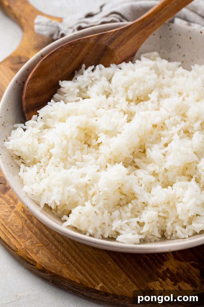 Angled photo of Instant Pot jasmine rice with a wooden spoon in a large bowl on a wooden tray with a cloth napkin