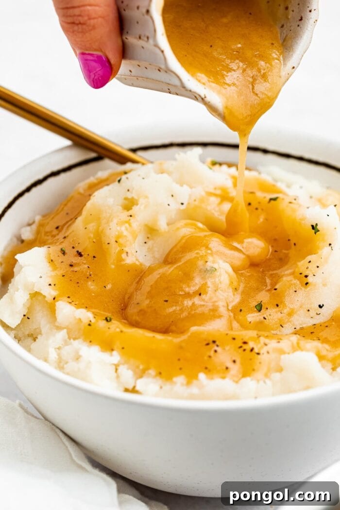 Rich, golden-brown keto gravy being generously poured into a bowl of creamy mashed cauliflower, highlighting its smooth, luscious texture and appetizing warmth.