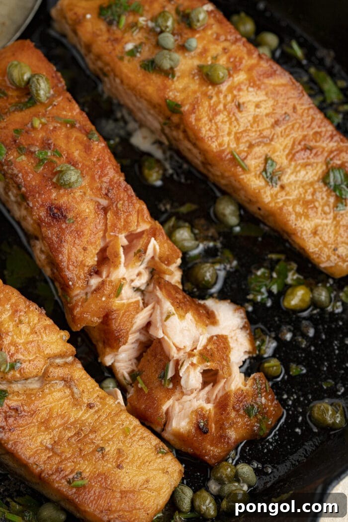 A close-up view of a pan-fried salmon meuniere fillet garnished with fresh parsley, sitting in a cast iron skillet, ready to be served.