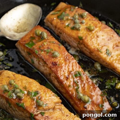 Salmon meuniere in a cast iron skillet with parsley and lemon wedges