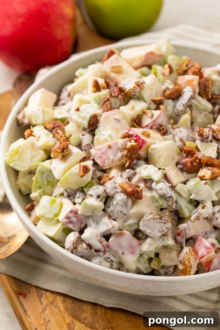 Slightly zoomed out shot of apple salad in a large bowl, with whole apples in the background, ready to be served.