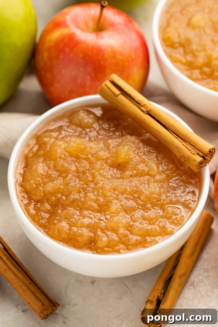 Instant Pot applesauce in a large bowl surrounded by apples and topped with a whole cinnamon stick