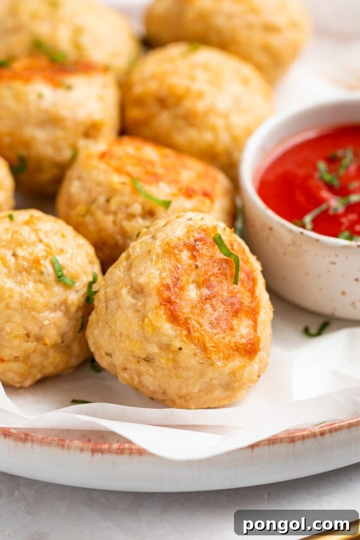 Golden-Brown Chicken Meatballs 2 Close-up image of golden-brown baked chicken meatballs on a plate, with a side of vibrant tomato sauce, ready for dipping and serving.