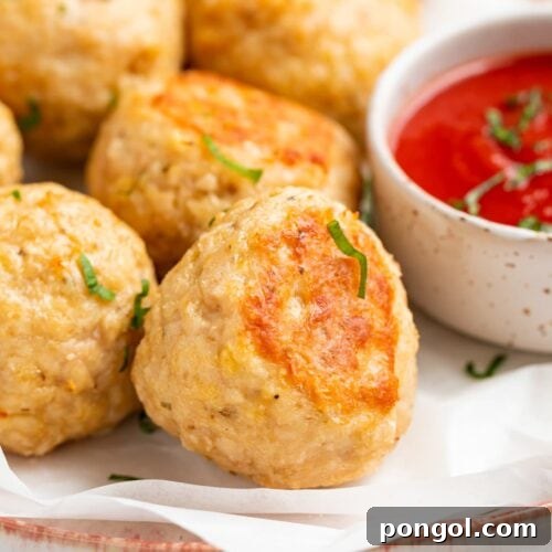 close-up image of baked chicken meatballs on a plate with tomato sauce on the side