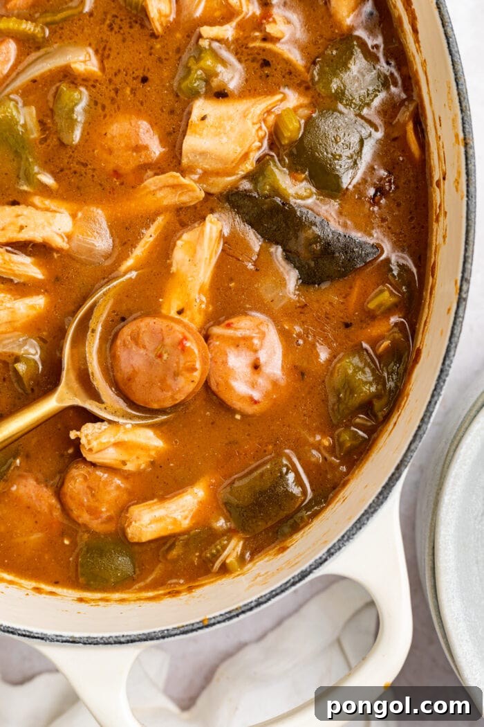 Large pot filled with simmering chicken and sausage gumbo, with a wooden spoon resting inside, ready to be served.