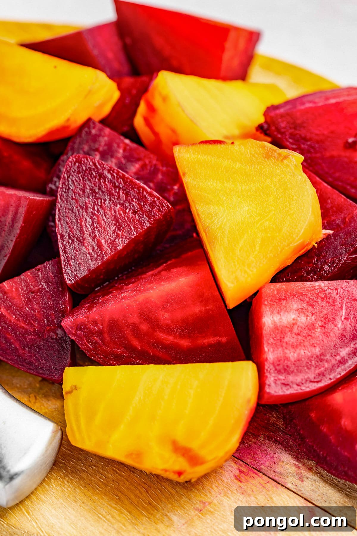Large chunks of red and yellow beets on a wooden cutting board, showcasing their vibrant colors and earthy appeal.
