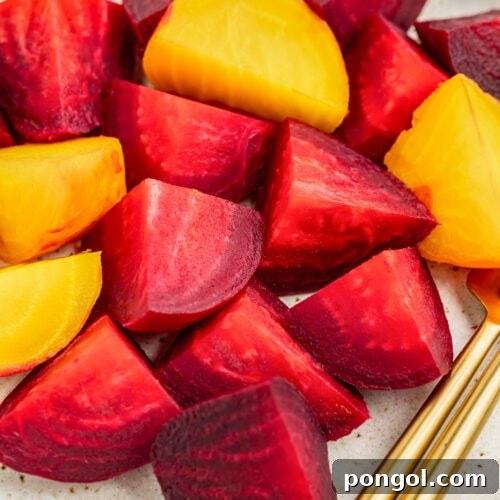 Zoomed out view of chunks of red and golden beets on a white plate with gold silverware.