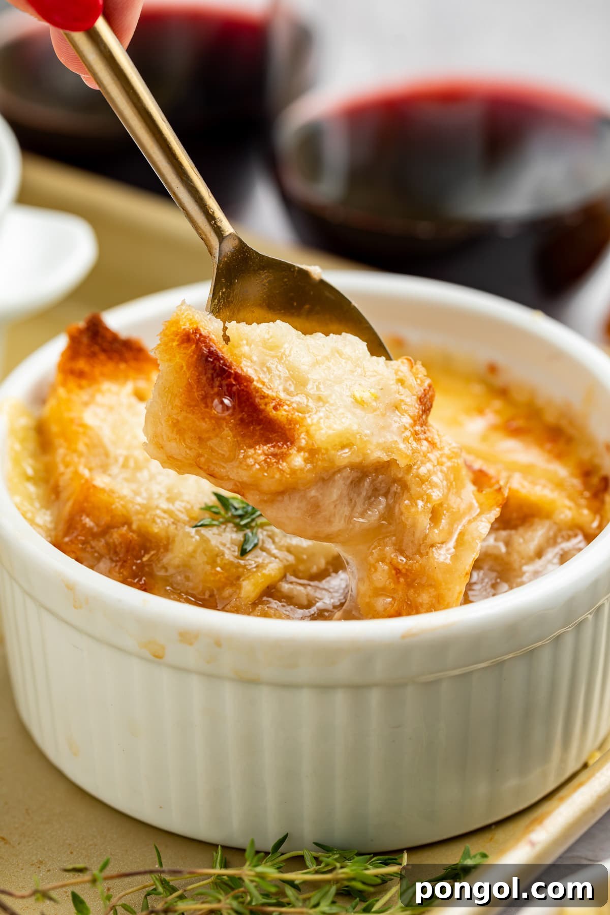 A spoon lifting a piece of French bread off the top of a ramekin holding Instant Pot French onion soup.