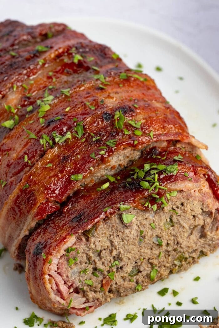 Overhead view of glistening bacon wrapped meatloaf with a sweet glaze, fresh parsley garnish, and a dollop of ketchup on a pristine white plate, ready to be served as a delightful family dinner.