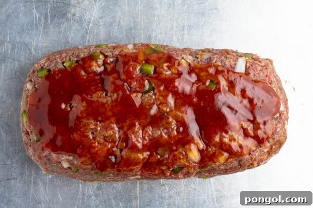 Uncooked meatloaf with glaze on baking sheet