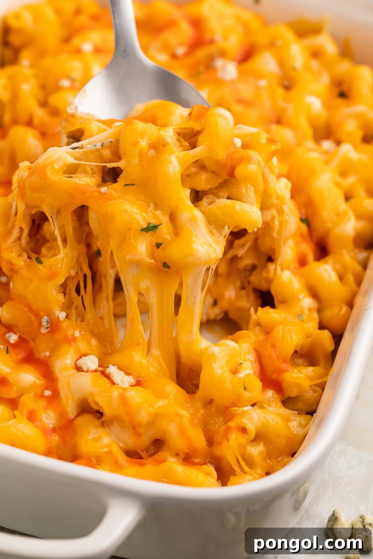 A large spoonful of orange buffalo chicken mac and cheese being lifted out of a casserole dish.