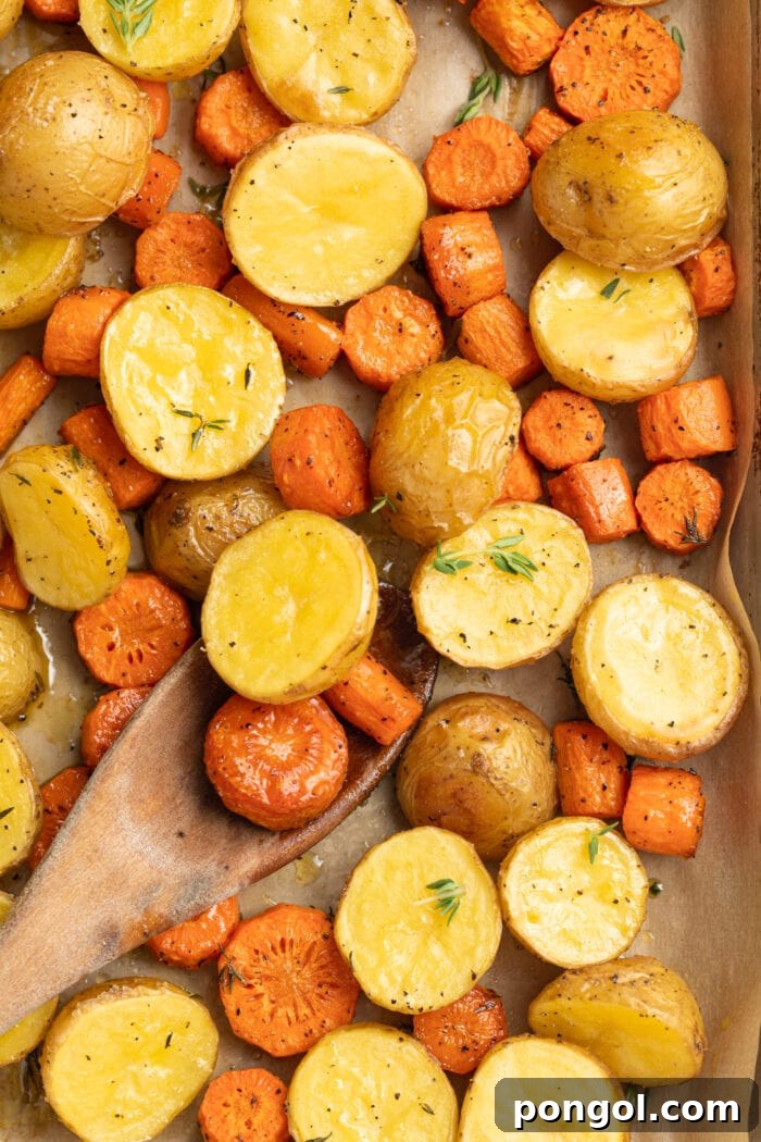 Roasted potatoes and carrots on a baking sheet with fresh thyme and a wooden spoon, ready to be served.