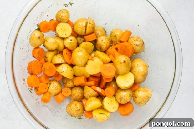 Potatoes and carrots tossed with olive oil and seasonings in a bowl.