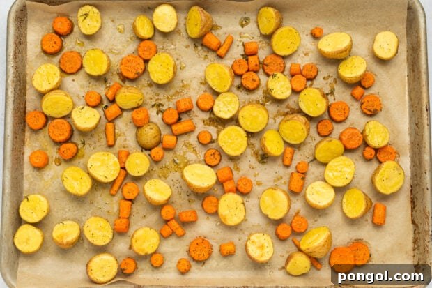 Roasted potatoes and carrots baking on a parchment-lined sheet.