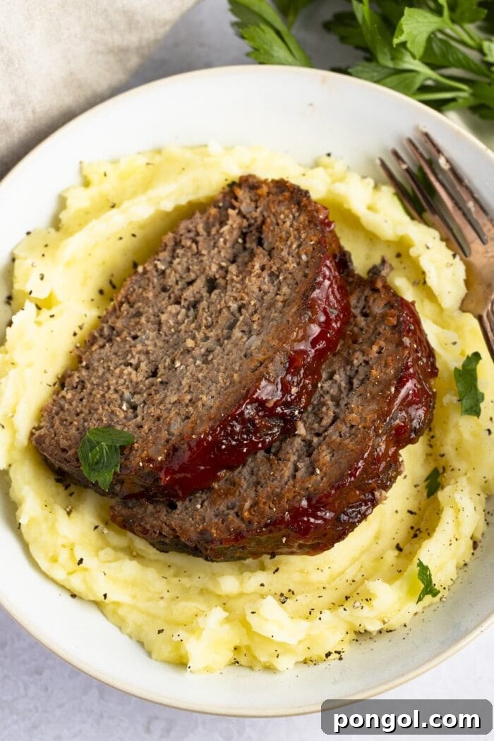 Effortless Slow Cooker Meatloaf 2 Two generous slices of tender slow cooker meatloaf, served atop a bed of creamy mashed potatoes, ready for a comforting meal.