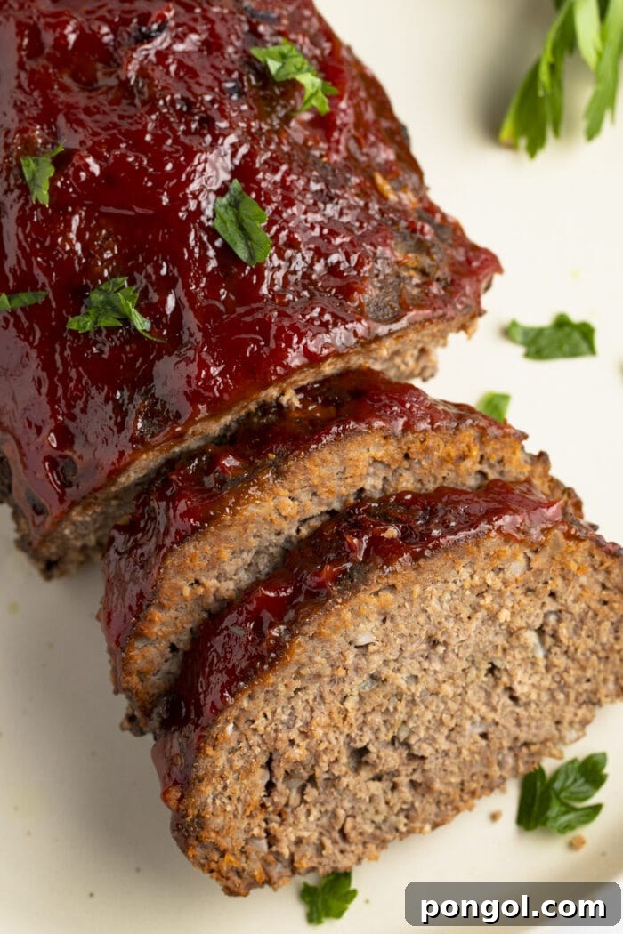 Effortless Slow Cooker Meatloaf 3 An overhead view of a perfectly cooked slow cooker meatloaf, with two slices neatly arranged against the main loaf on a pristine white plate, showcasing its tender texture.