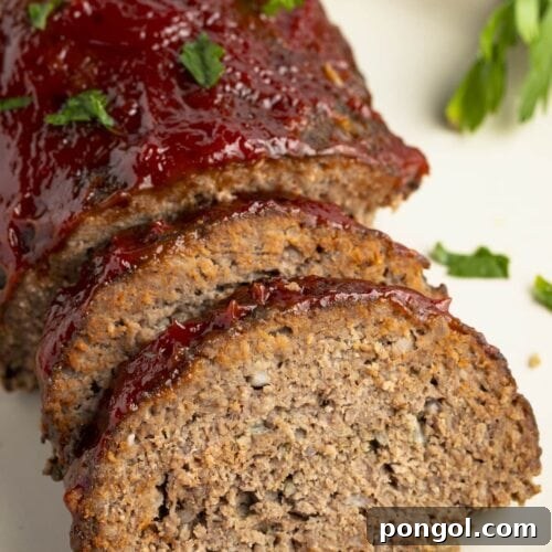 Slow cooker meatloaf, photographed from an overhead angle, with two slices leaning up against the end of the loaf on a white plate