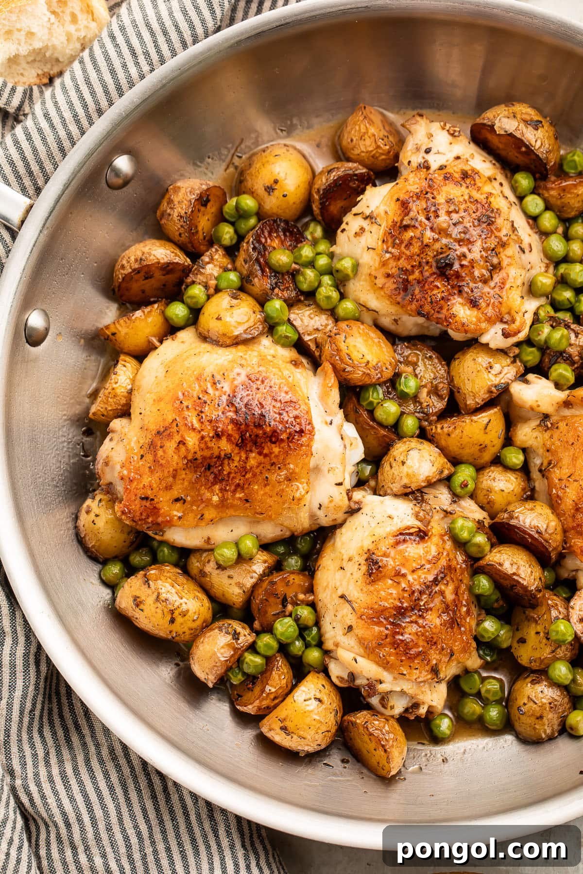 Close-up of golden-brown Chicken Vesuvio chicken thighs and roasted potatoes, glistening with sauce, in a silver skillet.