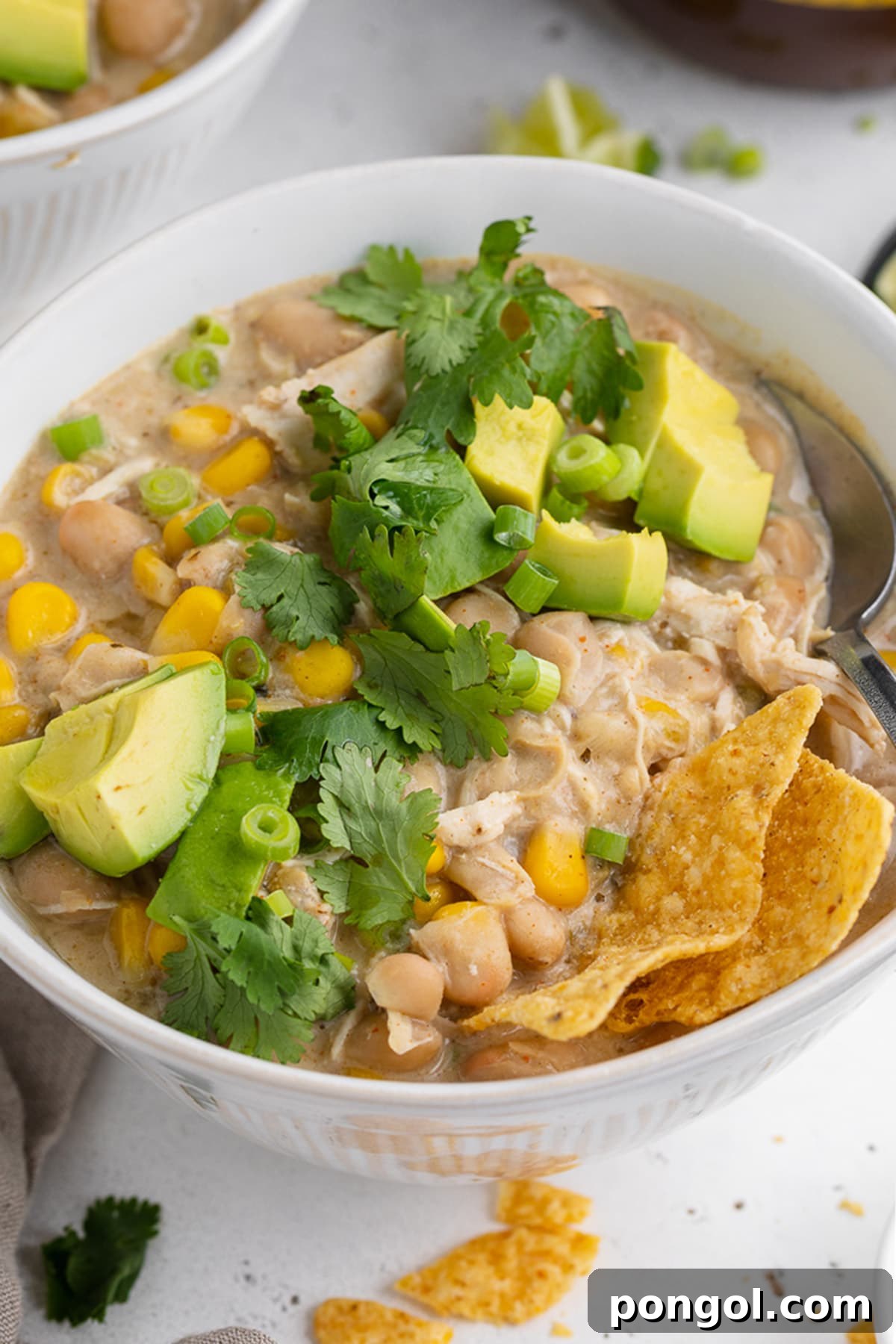 Effortless Instant Pot White Chicken Chili 3 Angled view of a bowl of Instant Pot white chicken chili topped with avocado, cilantro, and tortilla chips.