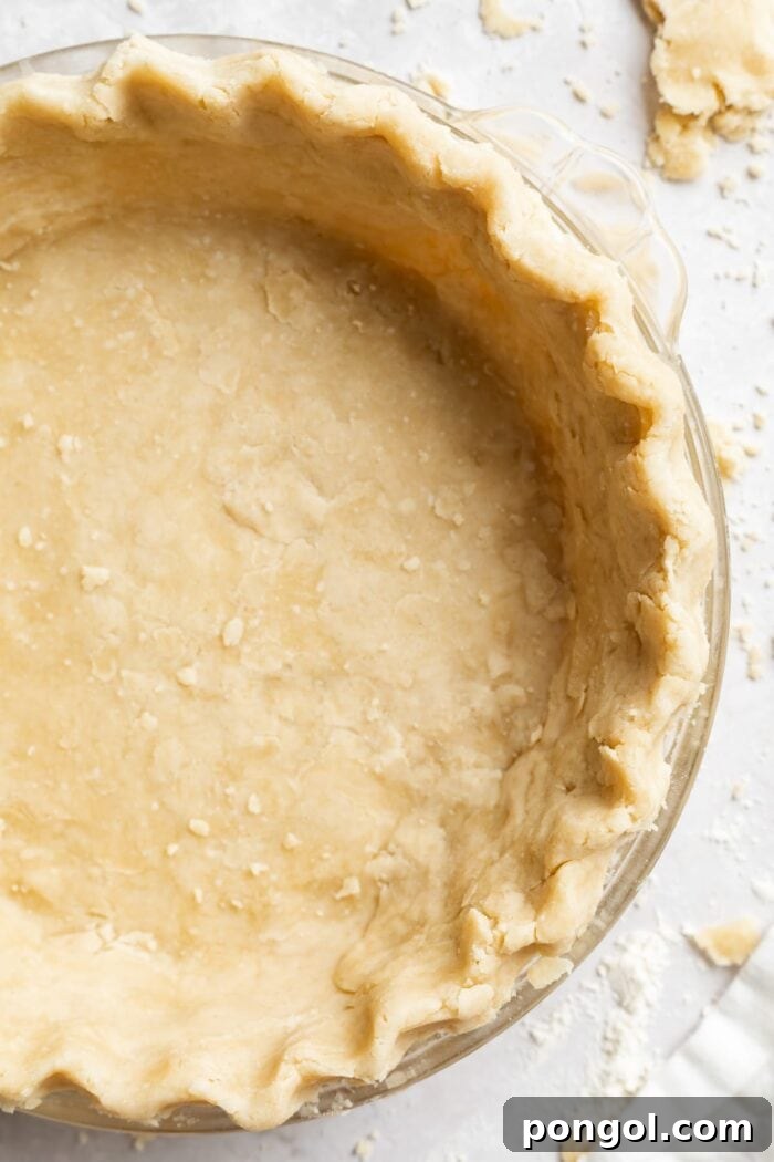 overhead image of vegan pie crust in a pie dish, golden and perfectly crimped