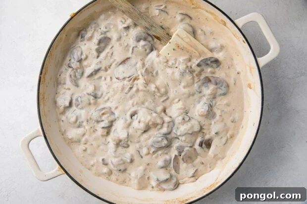 Mushrooms and onions coated in a rich, creamy sauce inside a large skillet, ready to be simmered.