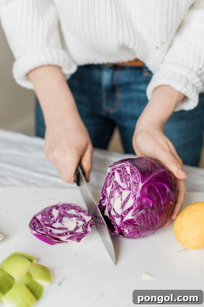 Your Ultimate Guide to Freezing Cabbage 4 A woman in jeans and a sweater cutting a head of purple cabbage on a kitchen counter