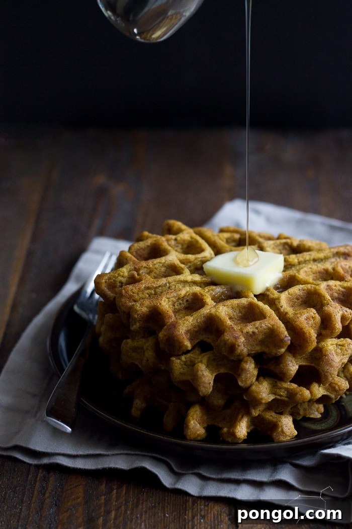 Golden-brown vegan pumpkin waffles, drizzled with maple syrup