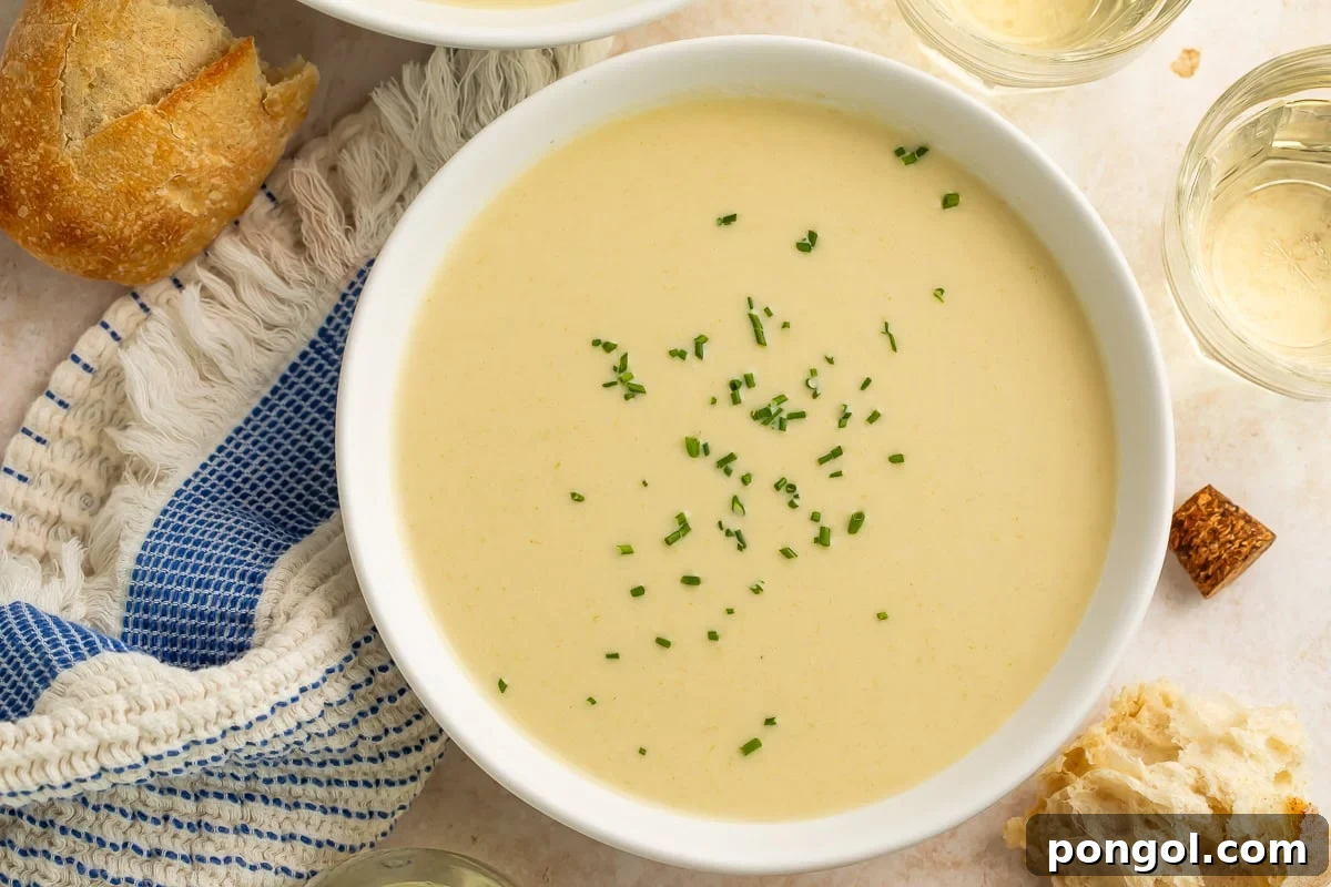 Homemade cream of celery soup in a white bowl, garnished with fresh chives, served with crusty bread and white wine.