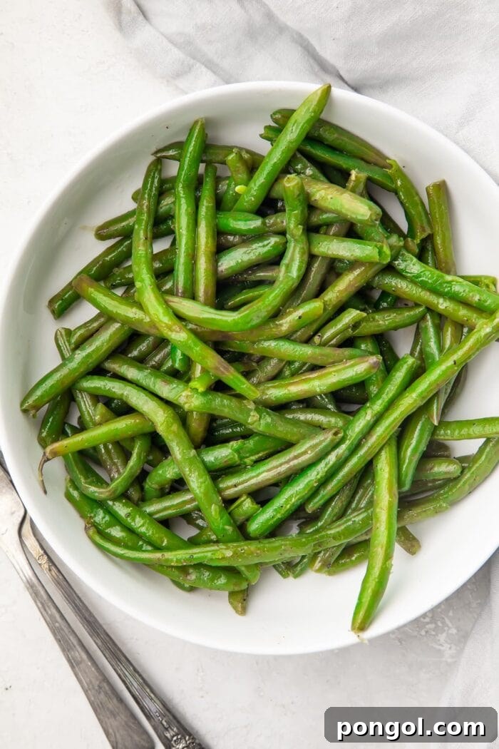 Overhead view of a large white bowl containing vibrant green Instant Pot green beans, garnished with herbs.