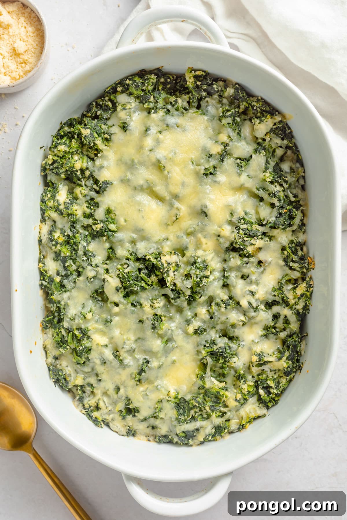 Top-down view of a large oval casserole dish holding a cheesy spinach casserole topped with golden parmesan and breadcrumbs.