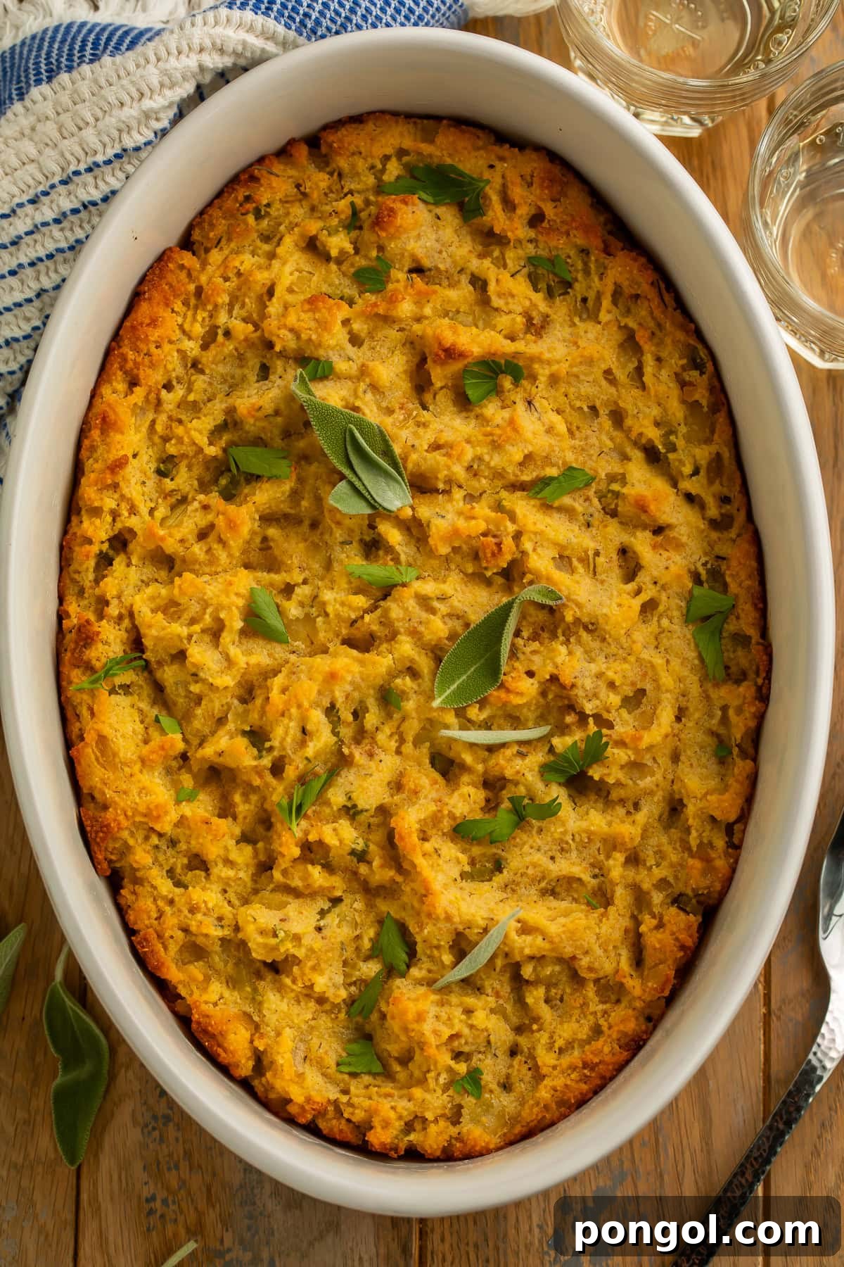 Overhead view of golden-brown cornbread stuffing in an oval baking dish with crispy edges, garnished with sage and parsley.