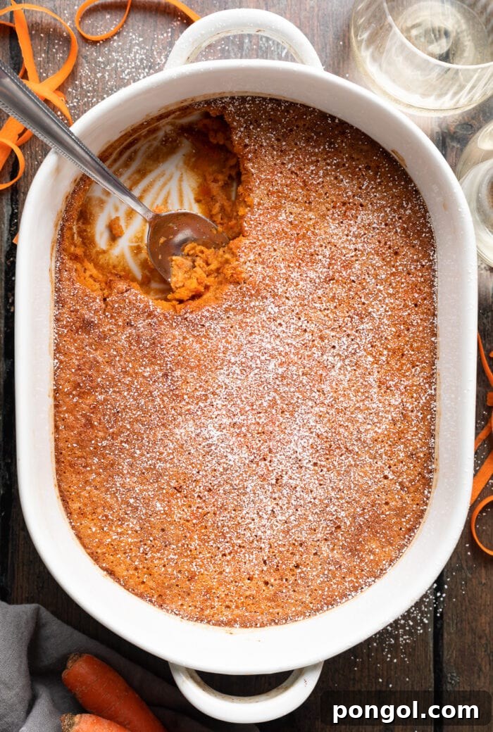 Overhead view of a golden-brown carrot soufflé in a white ceramic casserole dish, garnished with a light dusting of powdered sugar.