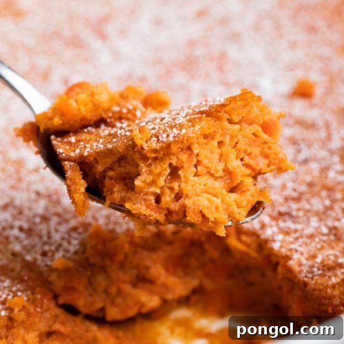 A serving spoon lifts a generous portion of warm, fluffy carrot soufflé from a baking dish, showcasing its soft texture and golden color.