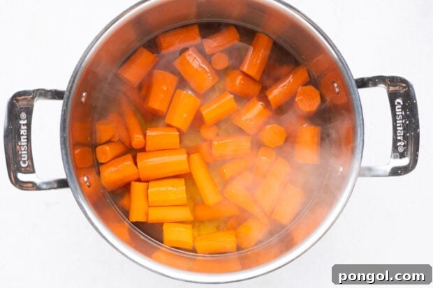 Chopped carrots boiling in a large pot of water on a stovetop, steam rising.