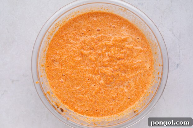 Close-up of carrot soufflé mixture being beaten in a large bowl with an electric hand mixer.