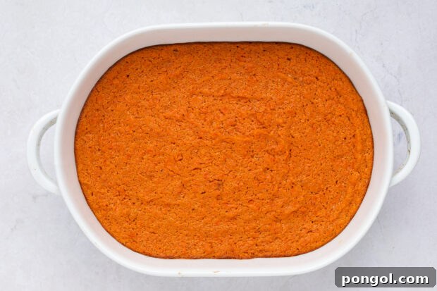 Unbaked carrot soufflé mixture poured into a glass baking dish, ready for the oven.