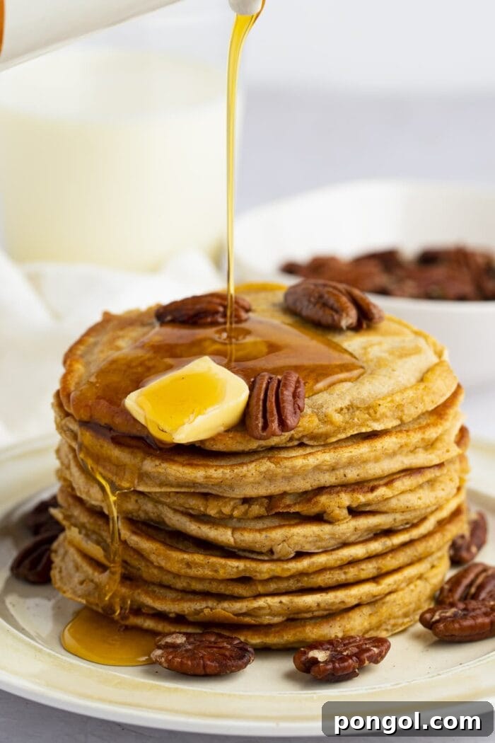 Golden maple syrup generously poured over a tall stack of fluffy sweet potato pancakes, adorned with toasted pecans and a dollop of melting butter.