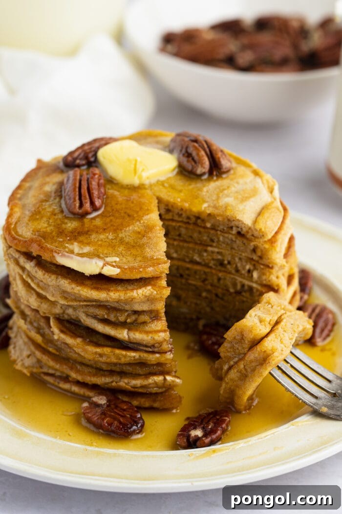 A slice of sweet potato pancake resting on a fork, showing the fluffy texture, with a stack of pancakes topped with roasted pecans and butter in the background.