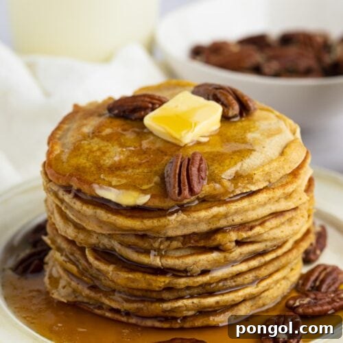 A vibrant stack of sweet potato pancakes, perfectly golden, topped with toasted pecans, a melting pat of butter, and a generous drizzle of maple syrup.