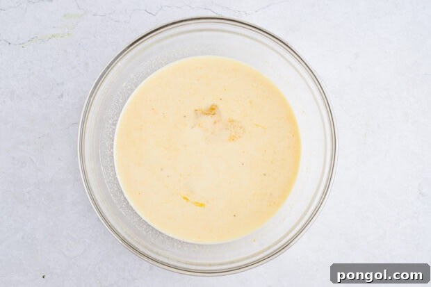 Wet ingredients for sweet potato pancakes in a large glass mixing bowl, showing the mashed sweet potato, milk, vanilla, and eggs.