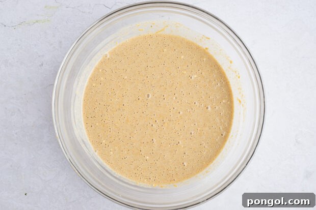 Sweet potato pancake batter in a large glass mixing bowl, with a whisk showing its combined consistency.