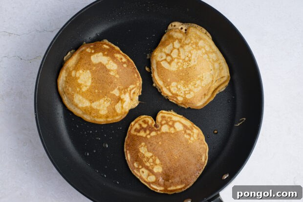 Sweet potato pancakes cooking on a skillet, showing their golden brown exterior.